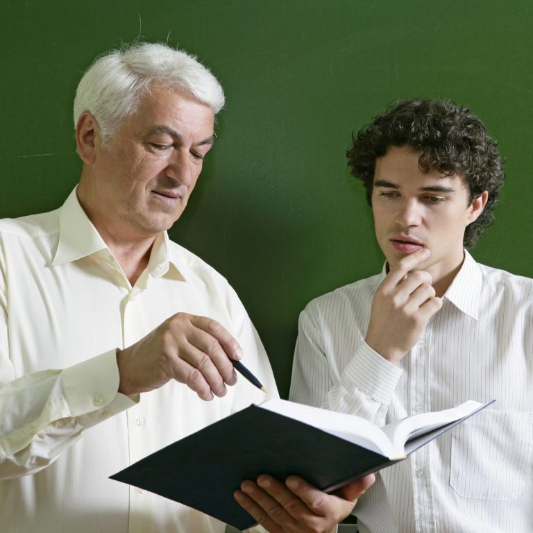 Einzelkurs Ein älterer Mann erklärt einem jüngeren Mann etwas aus einem Buch.