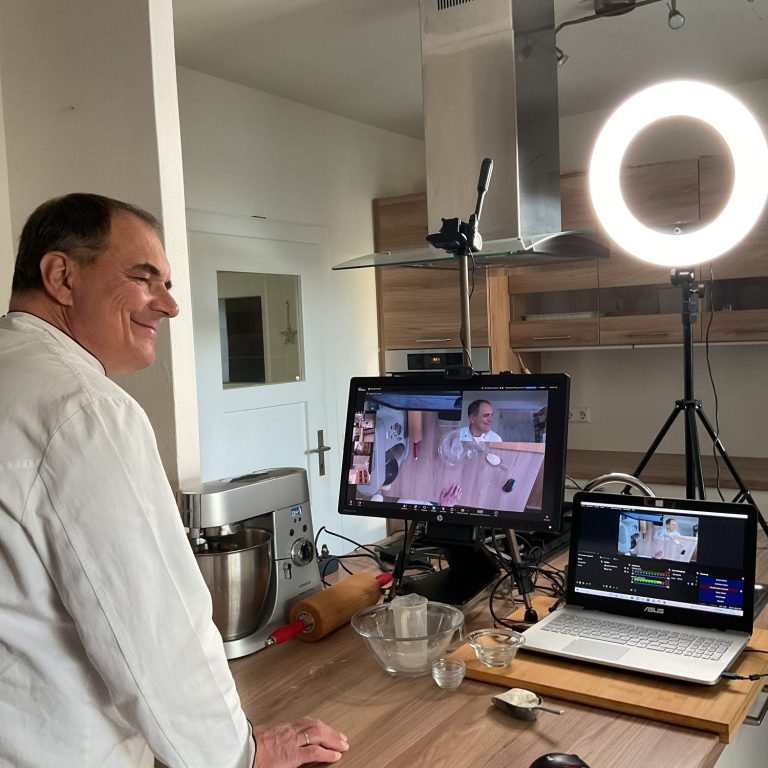 Kurssituation Ein Bäcker steht an einer Arbeitsplatte mit Laptop und Computer